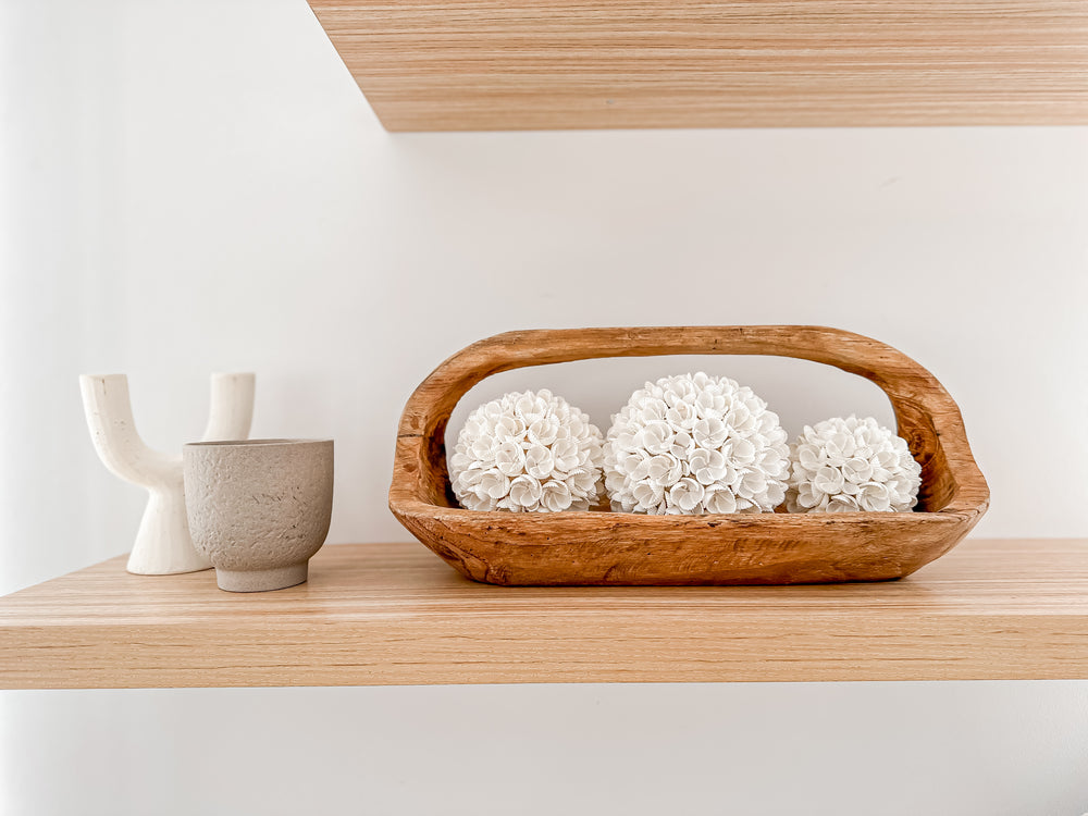 Wooden teak oblong basket with handle containing three sizes of white shell balls