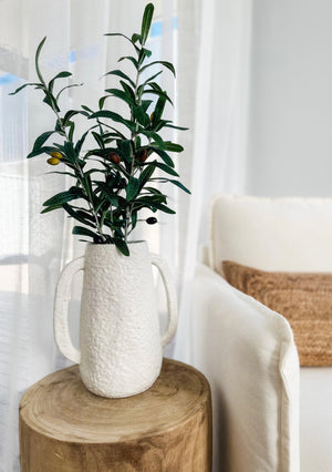 tuscan vase displayed with olive branches on top of wooden stool