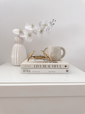 Small textured vase with two handles displayed on books with brass crab and vase of flowers