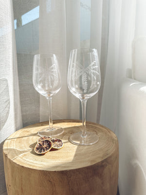 Clear wine glasses with an etched white palm tree displayed on a wooden stool