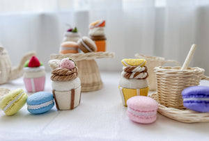 Table set with cupcakes, macarons on a cake tray with various cakes  displayed on table alongside a rattan teacup/saucer/spoon and a teapot