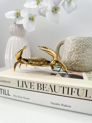close up of brass crab displayed on two books with a small vase containing flowers
