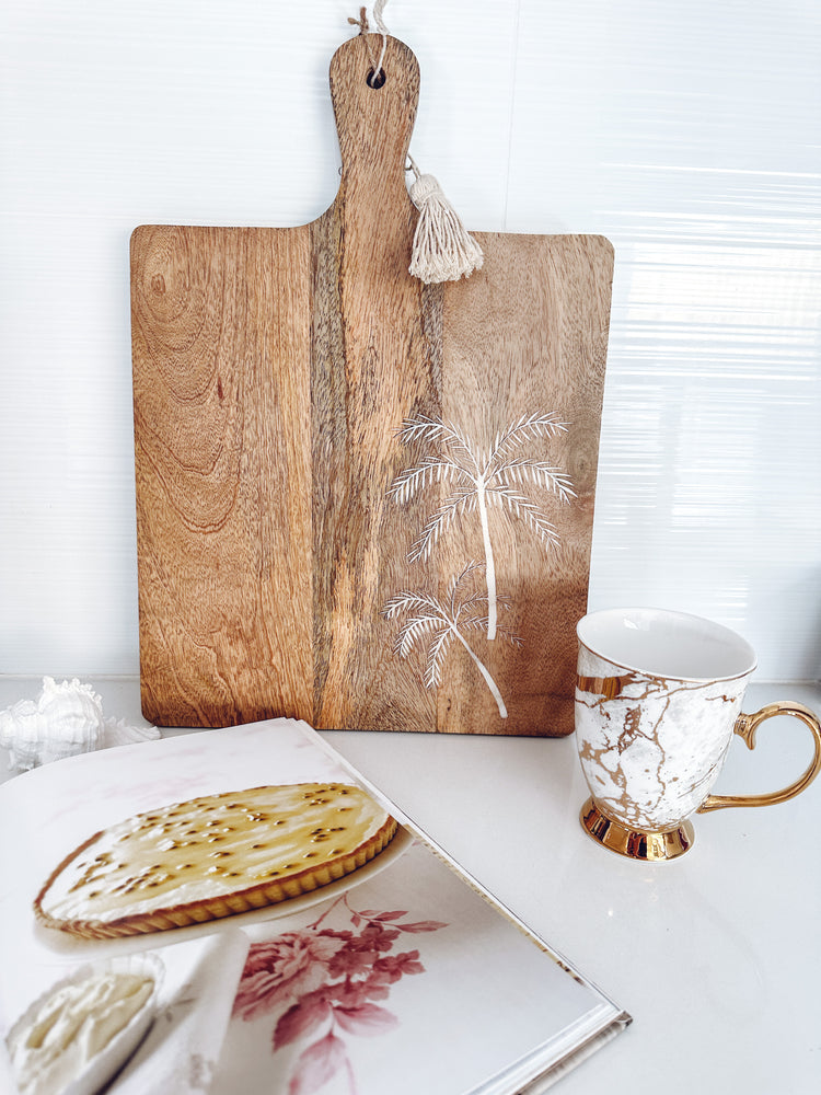Wooden paddle with etched palm trees and a tassel displayed in kitchen