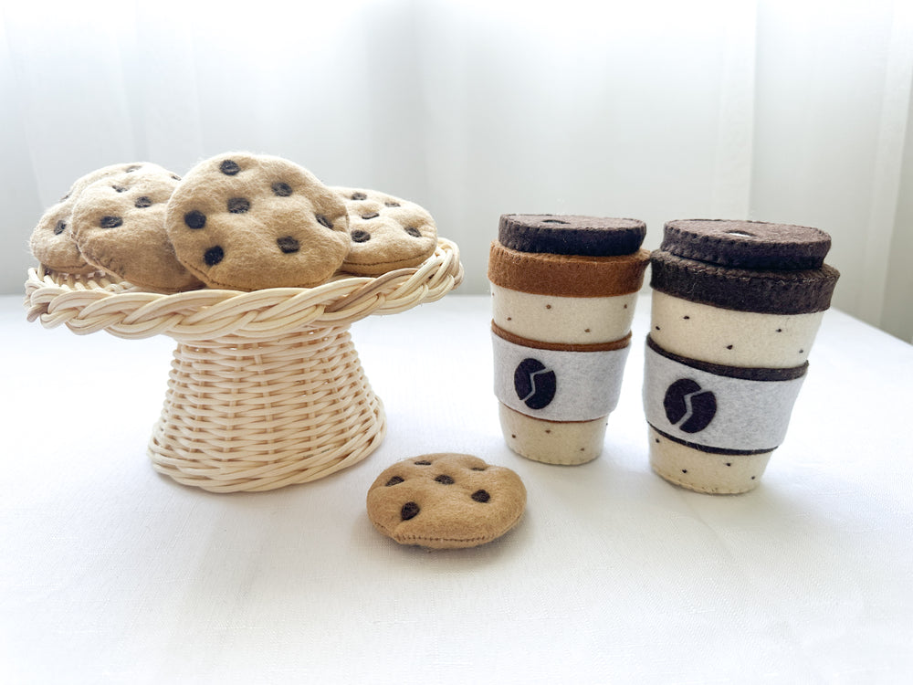 Two felt coffee cups with lids in mocha and latte colours with a chocolate chip felt cookies in rattan cake stand and one beside coffee cup.