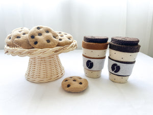 Two felt coffee cups with lids in mocha and latte colours with a chocolate chip felt cookies in rattan cake stand and one beside coffee cup.