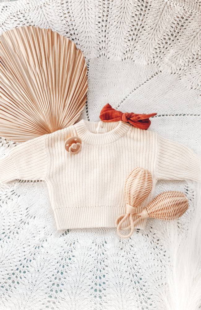 two rattan baby rattles displayed with baby outfit