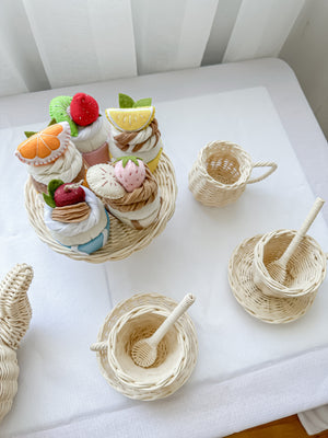 Set of five different coloured felt cupcakes  on a cake tray surrounded by a rattan teapot, milk jug and two sets of cups, saucers and spoons