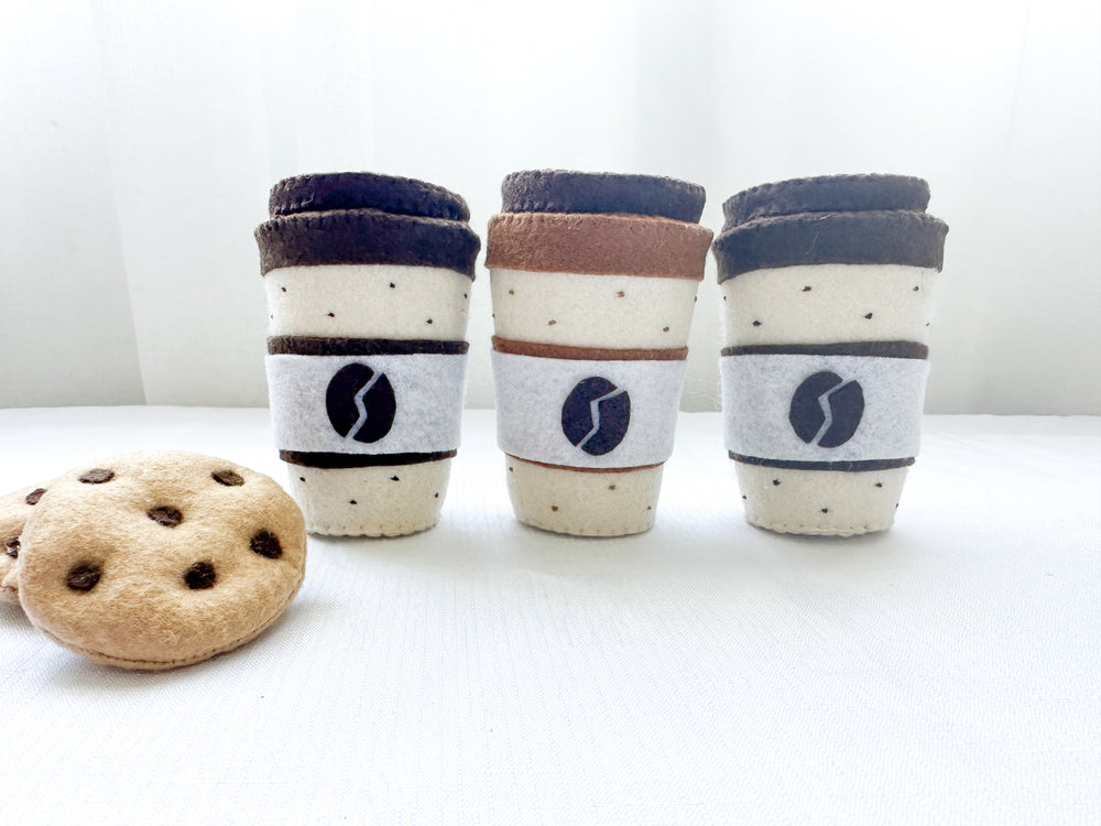 Three felt coffee cups with lids in mocha and latte colours with two chocolate chip felt cookies on the side.