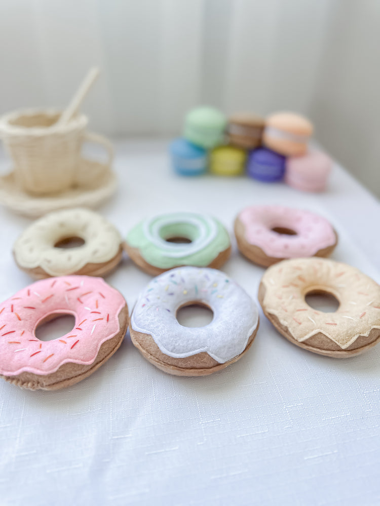 Set of six coloured donuts with macarons and a tea cup/saucer/spoon in the background