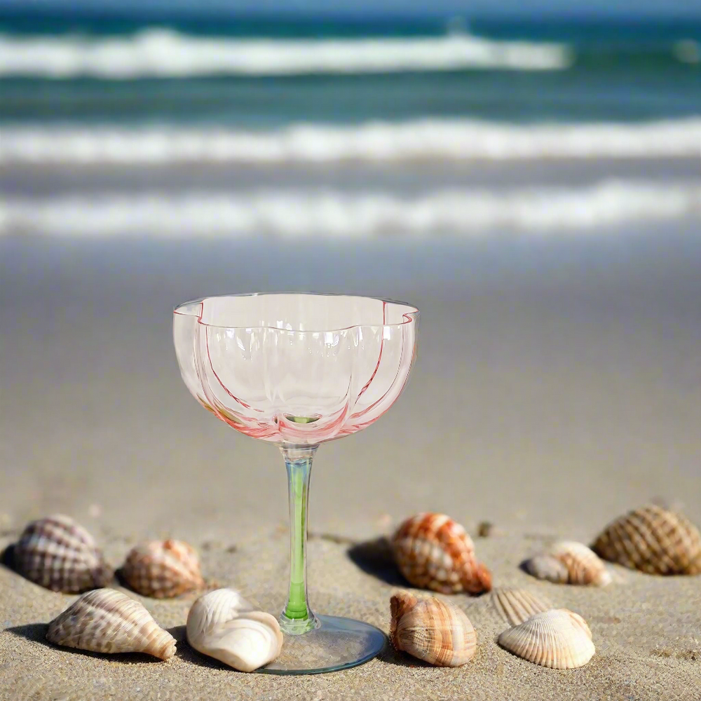 Pink Tulip glass on the sand with sea shells and sea in the background