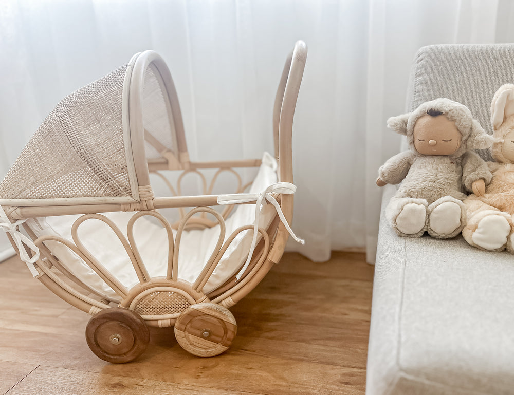 Rattan play dolls pram Violet in home interior with dolls on couch - handmade Balinese artisan toy with premium teak wheels for imaginative play ages 3+