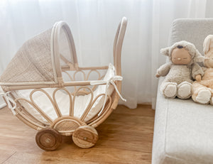 Rattan play dolls pram Violet in home interior with dolls on couch - handmade Balinese artisan toy with premium teak wheels for imaginative play ages 3+