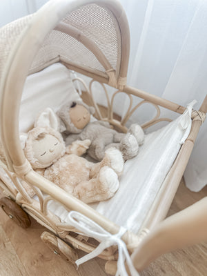 Close-up of rattan play dolls pram Violet with two dolls inside - handmade Balinese artisan toy with foam linen insert and teak wheels for imaginative play