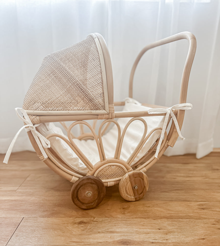 Rattan play dolls pram Violet with foam insert on wooden floor in natural light - handmade Balinese artisan children's toy with teak wheels