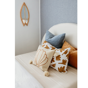 Rattan surfboard mirror on bedroom wall with cushion display on bed