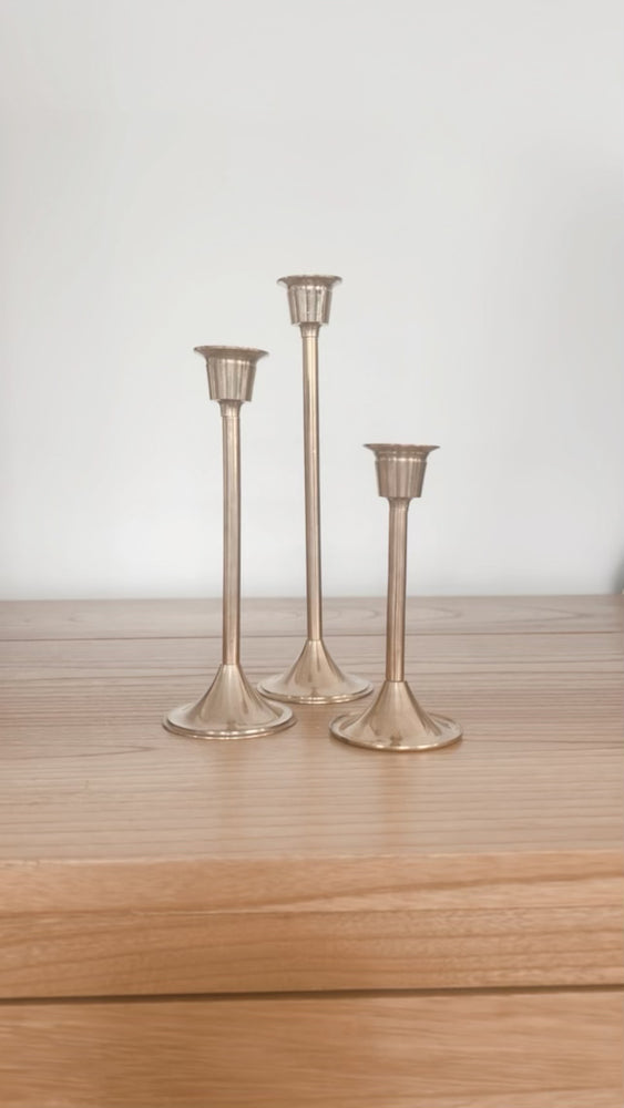 Set of three brass candleholders displayed on unit