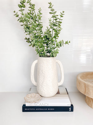tuscan vase displayed with olive branches on top of books
