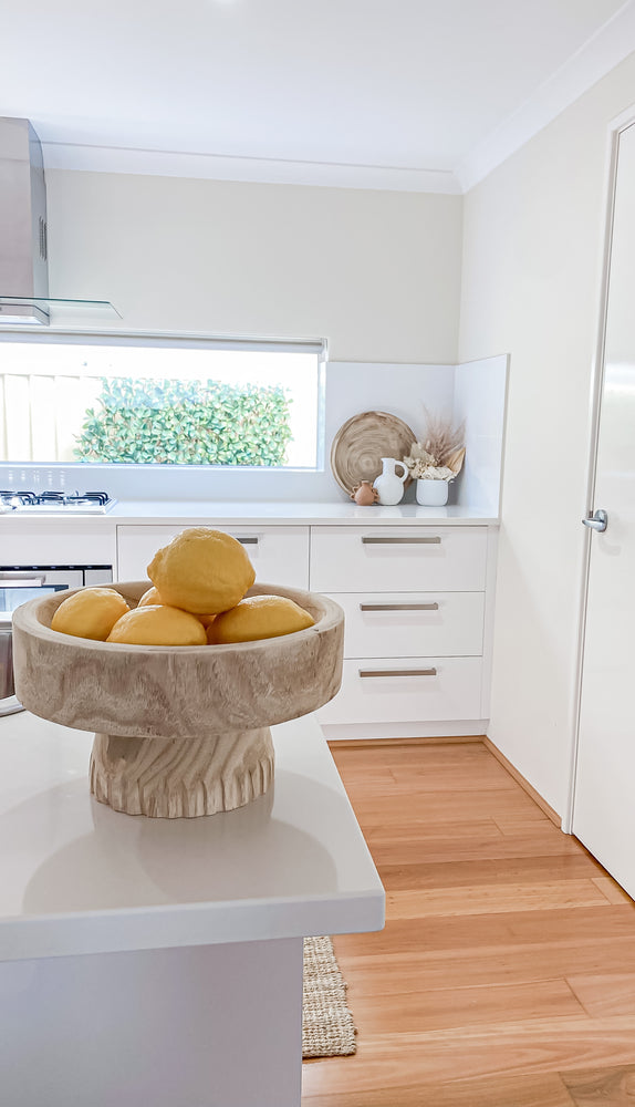 round paulownia wooden bowl on stand containing lemons displayed in kitchen area
