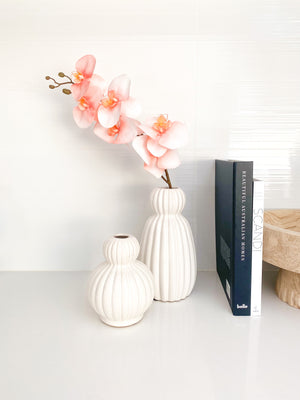 small white ceramic vase displayed with large white ceramic vase beside decoration books 
