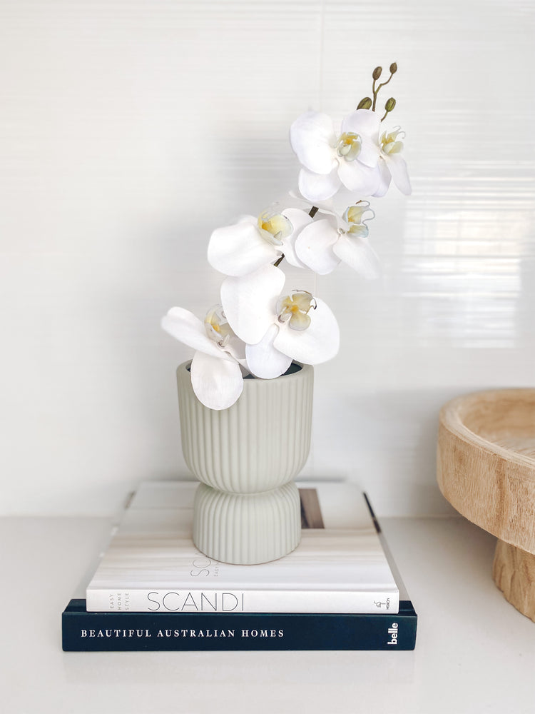 Grey ribbed ceramic vase displaying flower on top of books