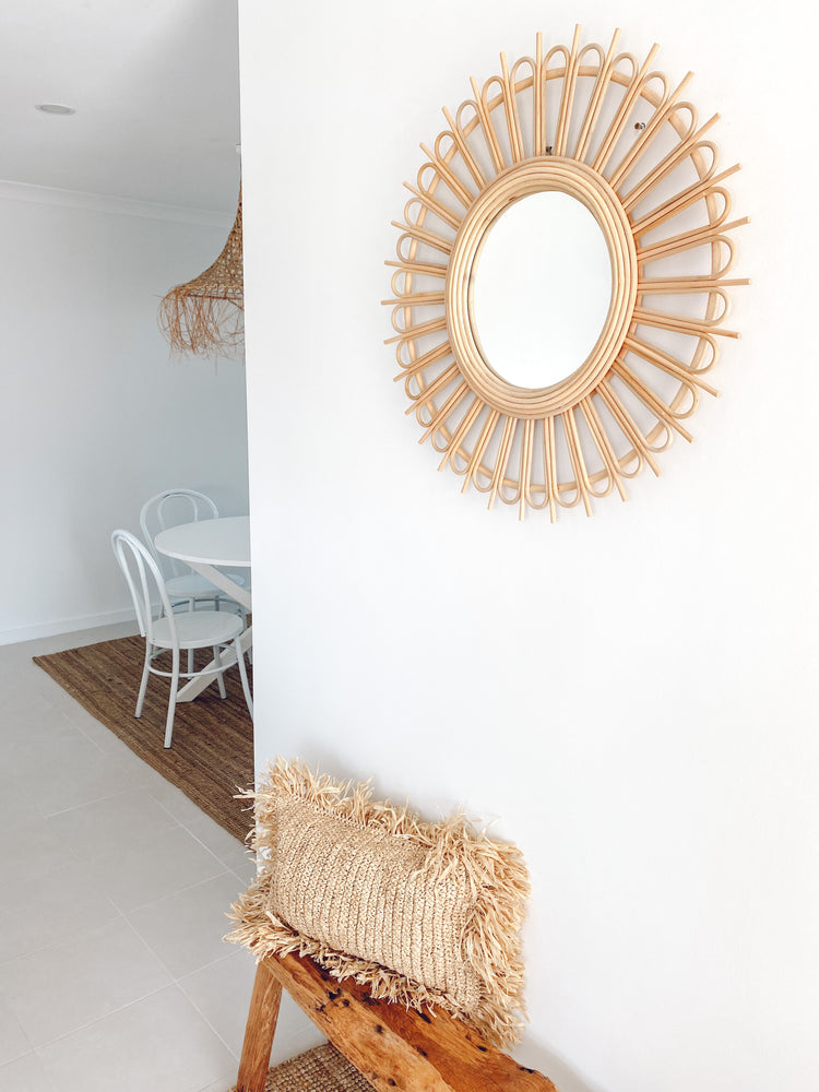 Rattan Starburst mirror displayed on wall over wooden bench