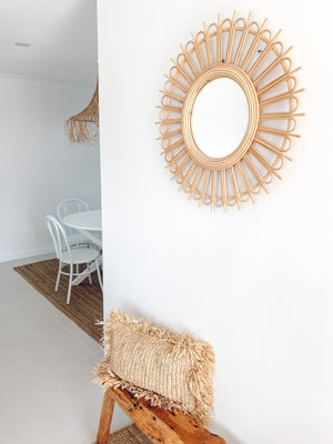 Rattan Starburst mirror displayed on wall over wooden bench