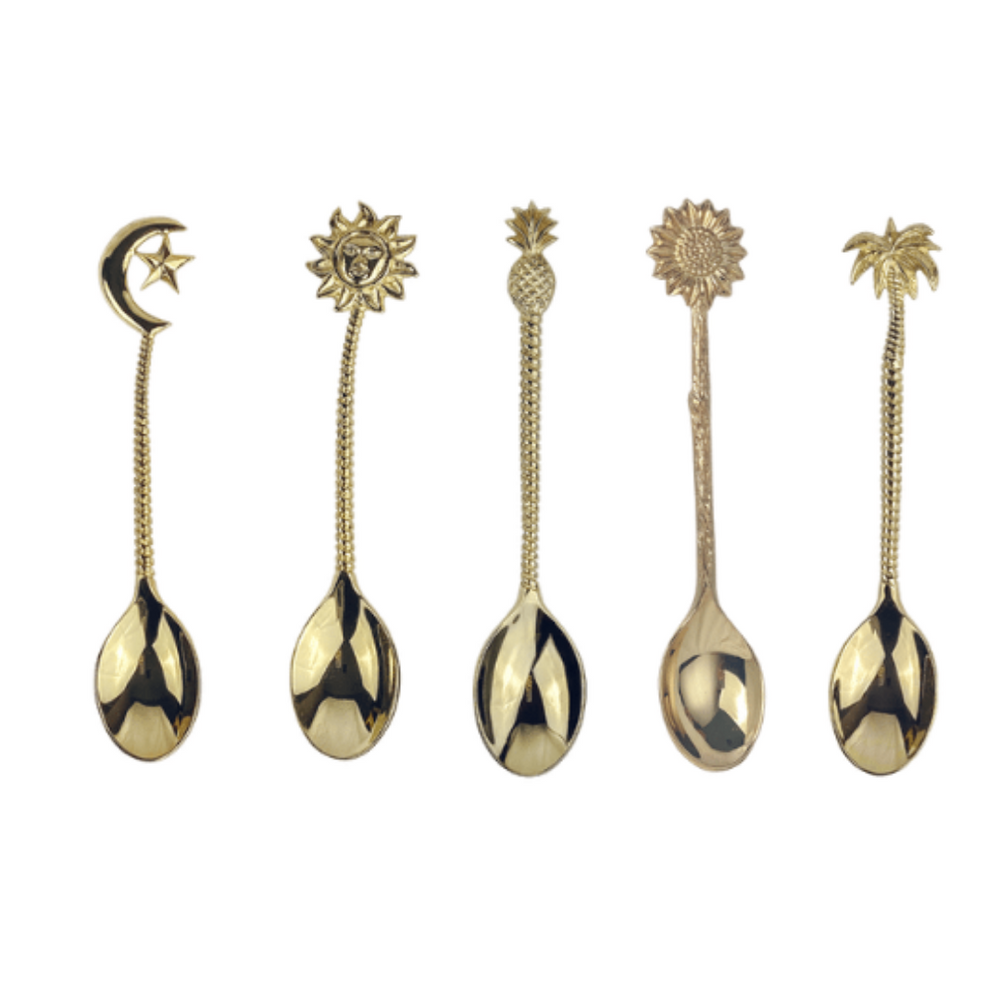 A selection of handmade brass spoons with various designs, including a flower, sun, moon, star, palm tree, and pineapple, each with a golden hue.