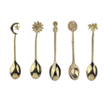 A selection of handmade brass spoons with various designs, including a flower, sun, moon, star, palm tree, and pineapple, each with a golden hue.
