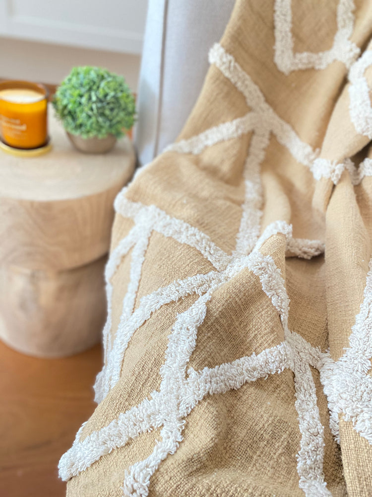 Cotton tufted throw in butterscotch colour on couch with wooden stool containing home decor products